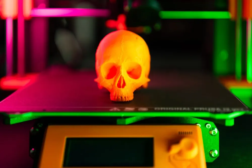 Orange 3D printed skull on a printer under neon light